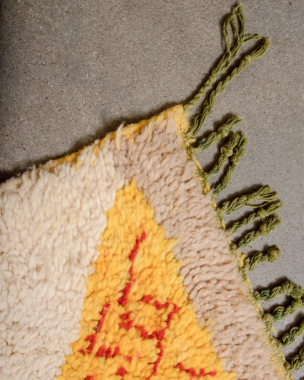 Corner of wool Boujad rug featuring green wool tassels, laying on concrete floor.